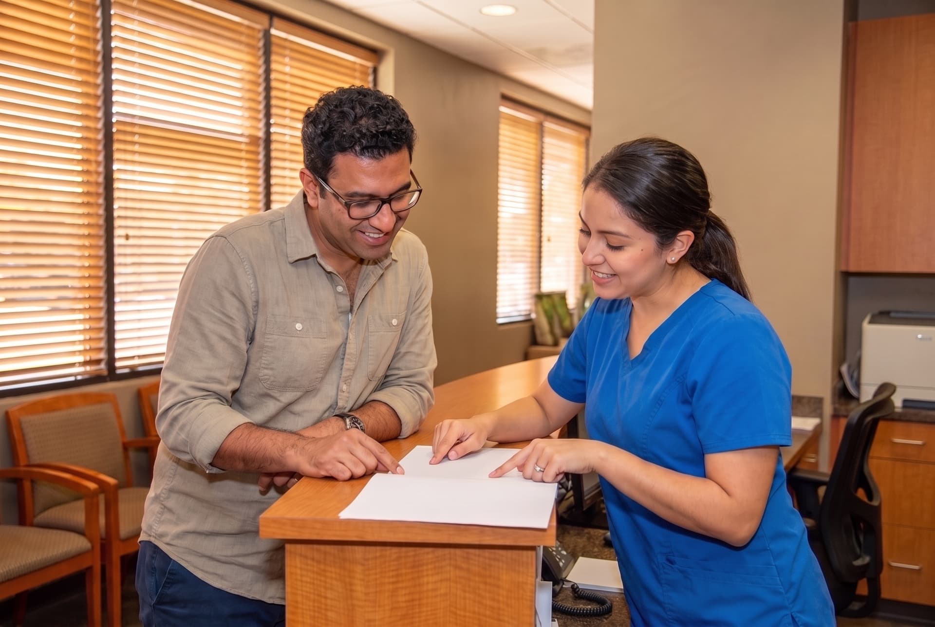 A patient and a team member at the reception counter, both looking down at a form on the counter between them