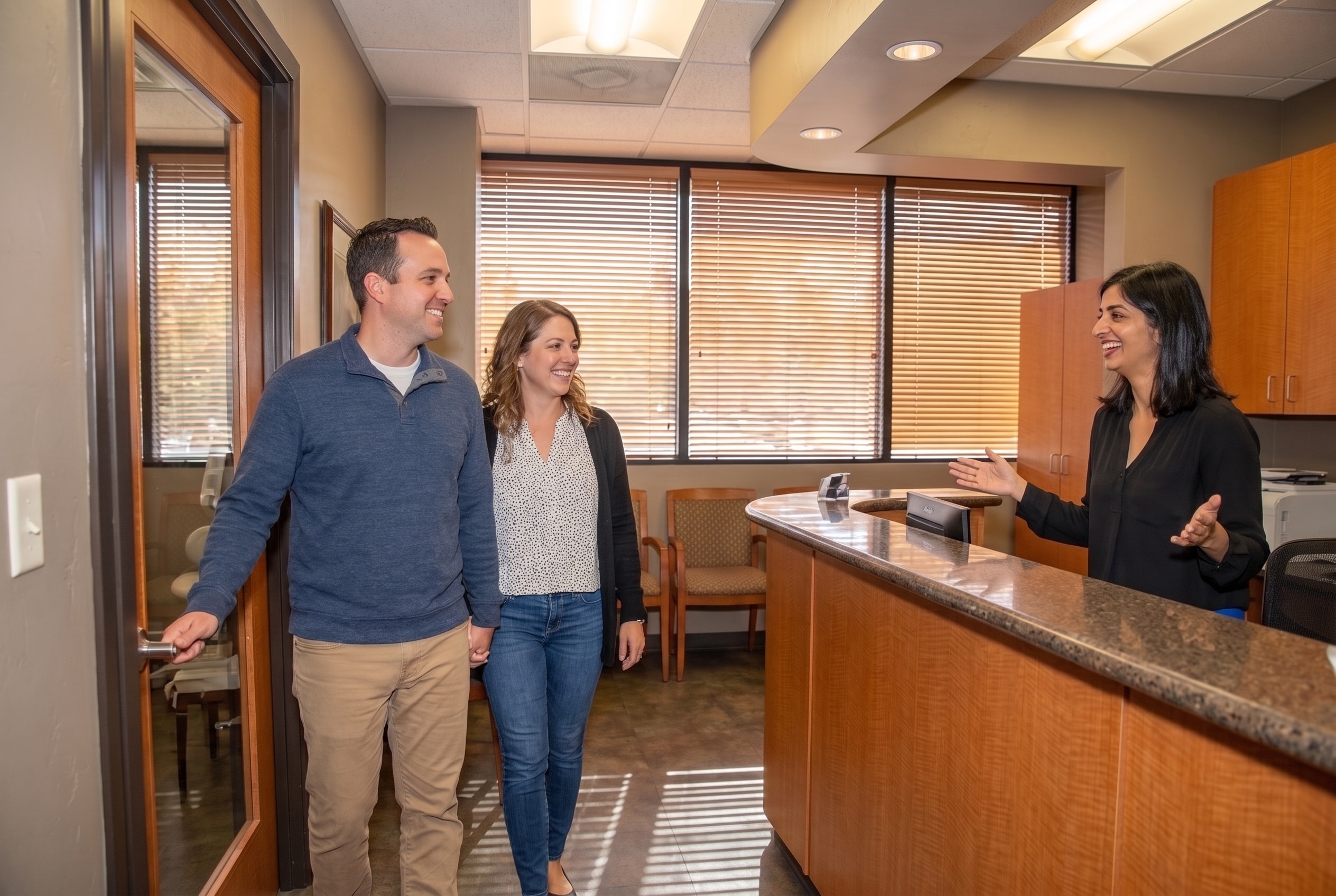 A receptionist greeting a couple as they arrive through the practice entrance