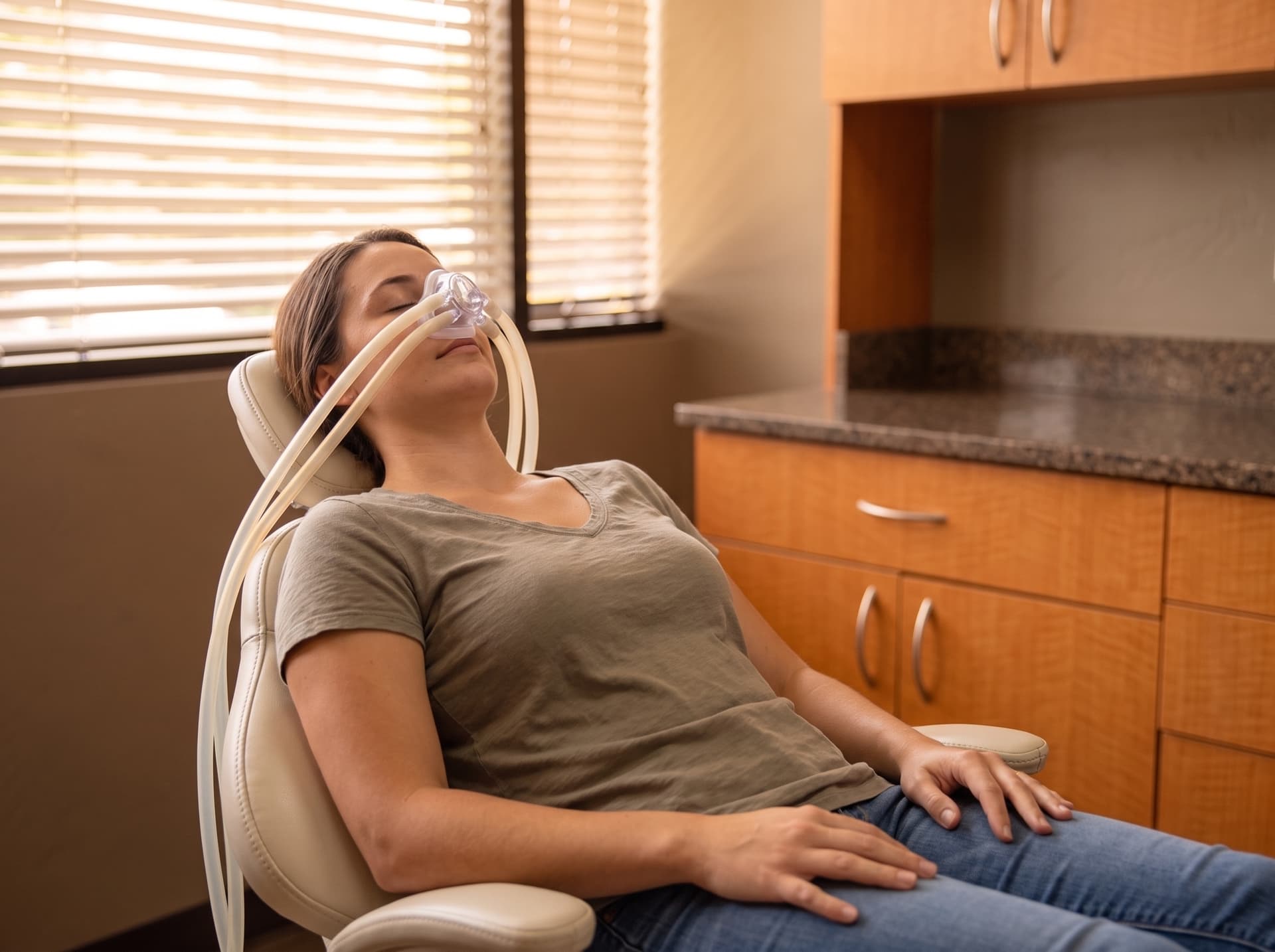 A patient reclined in the treatment chair wearing a small clear nasal hood, eyes closed and relaxed